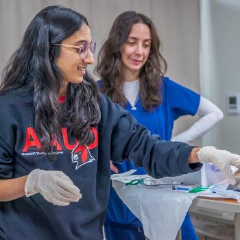 A female student practices catheterization on a manikin in a simulated hospital room.